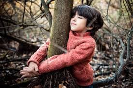 Niño feliz abraza un árbol dentro de un bosque, buen entorno para vivir el inglés.